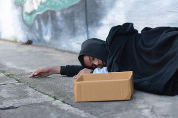 Asian teenager wearing black headscarves sleep on the outside wall of a building as they are...
