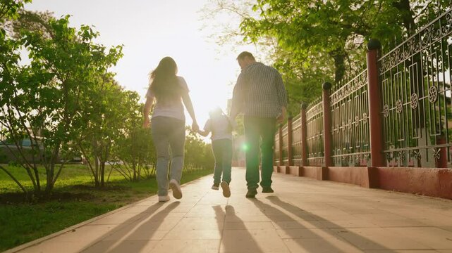 happy family. mother father child run through park sunset. mom dad kid fun running sun. view from back. happy family park. chidhood dream. family walk with kid around city playing. run teamwork