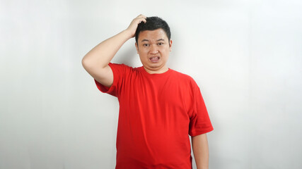 A young Indonesian man wearing a red t-shirt with a confused face facing forward