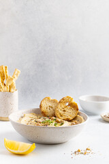 Hummus with olive oil in a gray ceramic plate. Toast and breadsticks for snacks.