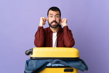 Traveler caucasian man with a suitcase full of clothes over isolated purple background frustrated...