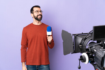 Reporter man holding a microphone and reporting news over isolated purple background thinking an idea while looking up