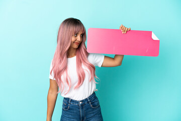 Young mixed race woman with pink hair isolated on blue background holding an empty placard