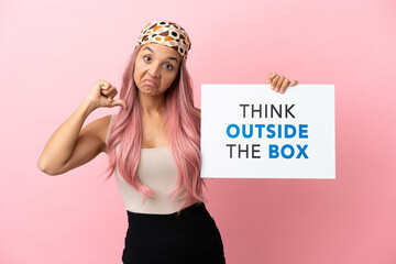 Young mixed race woman with pink hair isolated on pink background holding a placard with text Think...