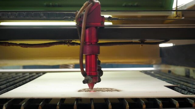 An industrial laser cuts a pattern on a sheet of plywood and moves close-up. Wood burning. Modern laser treatment of wood. A red laser beam passes through a tree.