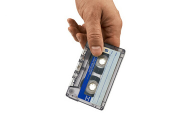 A close-up of a hand holding a vintage audio cassette tape with a blank label.