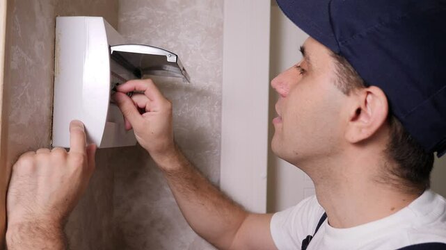 Close-up of an electrician opening a switchboard and inspecting fuses. An electrician repairs electricity in an apartment.