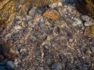reflections on stones of different sizes piled up on the bottom of the lake under water