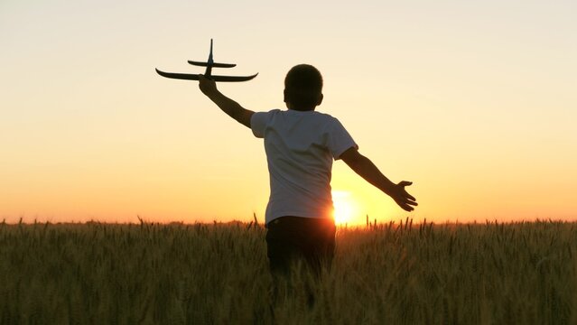 boy teenager child kid runs through field with wheat with toy plane his hands sunset, happy dream family, nature, dream astronaut sky, child dreams becoming pilot, kid run toy game by plane across