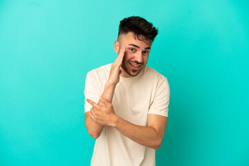 Fototapeta premium Young caucasian man isolated on blue background pointing to the side to present a product and whispering something