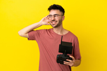 Man holding a drone remote control isolated on yellow background listening to something by putting hand on the ear