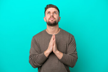 Young caucasian man isolated on blue background keeps palm together. Person asks for something