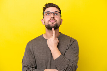 Young caucasian man isolated on yellow background With glasses and looking up