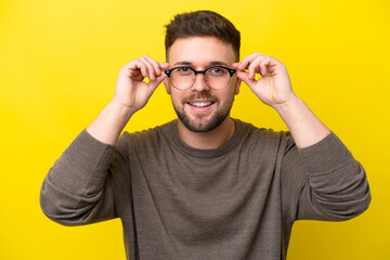 Young caucasian man isolated on yellow background With glasses with happy expression