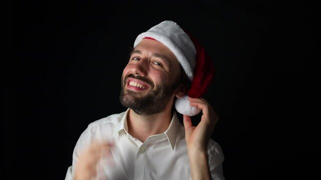 A young Caucasian man in a white shirt smiles at the camera while wearing a Christmas hat, having fun