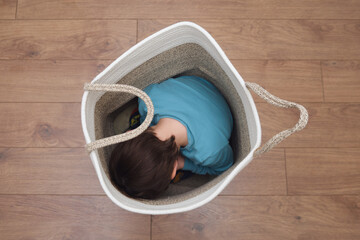 A sorrowful toddler baby hides alone in the basket, seeking a feeling of safety from his fears. The frightened child is curled up inside the basket, his filled with fear as he hides. Kid aged 3 years