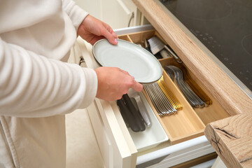 Person placing a plate into a kitchen drawer with organized cutlery and utensils. Indoor kitchen organization concept for storage and home design.