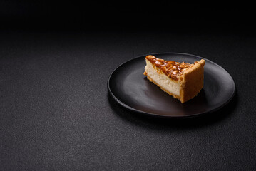 Delicious fresh cheesecake caramel peanut cake with cream and nuts on a ceramic plate on a dark concrete background