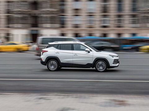 JAC JS4 driving on city highway, white compact crossover panning shot