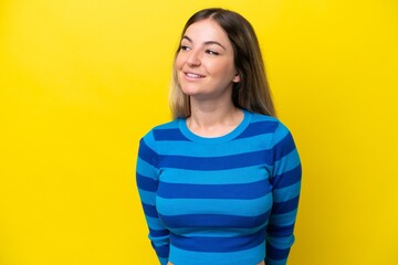 Young Rumanian woman isolated on yellow background looking to the side and smiling