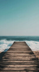 Fototapeta premium A wooden pier extends out into the blue ocean, with waves crashing around it. The sky is clear and bright, making for a peaceful scene