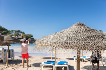 Unrecognizable tourist taking pictures with his cell phone on the beach of Cala Blanca, Menorca, Spain