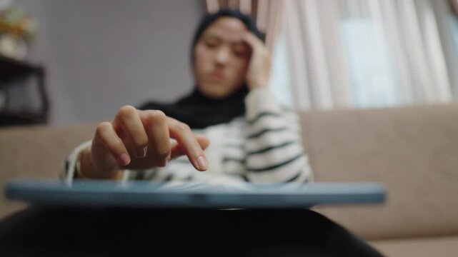Portrait of a woman in hijab feeling burnt out by work demands. Reading bad news and negative social media comments with an expression of disappointment and anxiety.