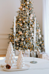 Elegant holiday decor featuring white trees and candles by a Christmas tree