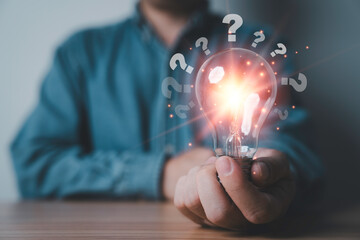Businessman hold glowing lightbulb with questions mark symbol for creative thinking idea and problem solving solution concept.