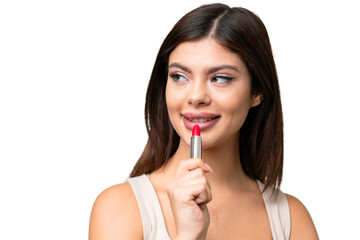 Young Russian woman with rainproof coat and umbrella over isolated chroma key background holding red lipstick