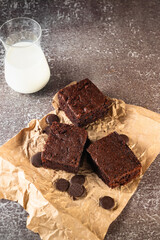 Chocolate brownie on paper and glass of milk on dark stone table. Homemade delicious chocolate pie