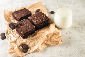 Chocolate brownie on paper and glass of milk on dark stone table. Homemade delicious chocolate pie