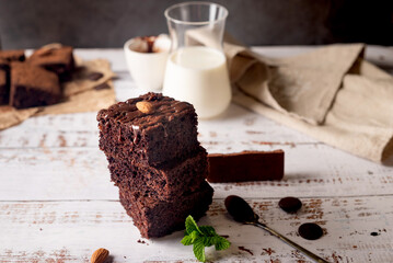 Chocolate brownies with melted chocolate topping, almond and leaves mint with glass of milk on table.