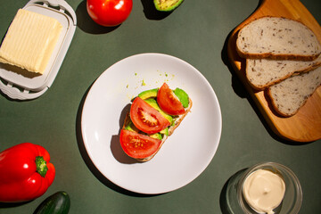 toast with tomatoes and avocado on from the white plate. Flat lay of the breakfast on dark green background. Traditional breakfast concept. Top view