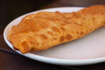 Chebureks with meat on a white plate on a wooden table. Big chebureks for dinner. Meat pies. A hearty lunch.