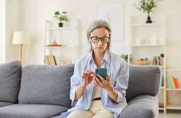 Elderly woman uses smartphone for online entertainment and communication at home. Engagement with digital technology, enjoying leisure and staying connected on the internet with phone.