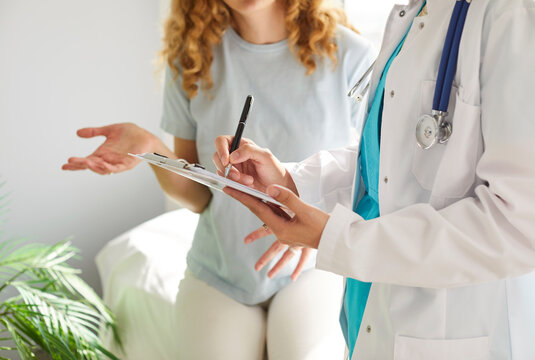 Doctor, nurse writing, looking at test result close up, discussing med anamnesis together with woman, medical professional thinking over treatment in hospital, clinic, talking, filling medical form