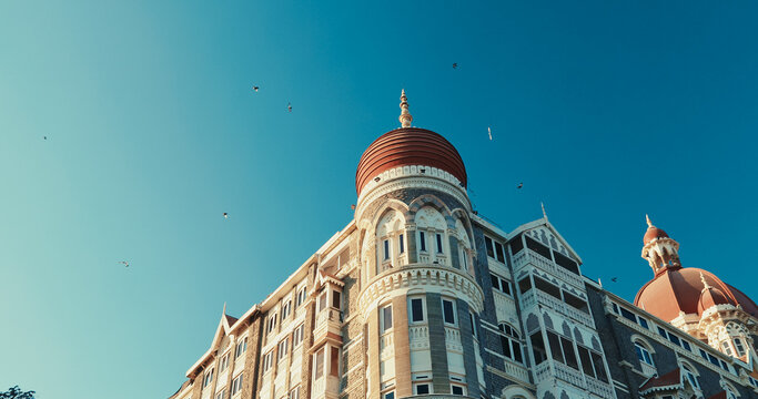 Mumbai, India. Blue Clear Sky In Sunny Day With Fly Pigeon Birds In Above Taj Mahal Palace. Finest Hotel In East. Close-up View On Taj Mahal Hotel Is Heritage, 