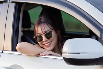 Asian woman wearing sunglasses, smiling and waving hand out of white car window. Capturing joy and excitement travel, road trip, car accident insurance, summertime, safe trip with rental car concept