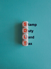 Wooden cubes with the word SDLT- Stamp duty Land Tax. Beautiful blue background. Business and buying housing and land concept.