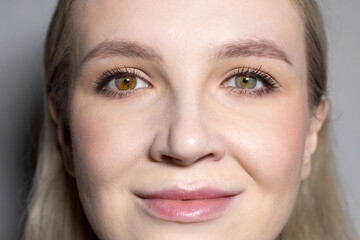 Close-up of the face of a young girl with heterochromia and light makeup on a gray background. Beauty and self-care concept. Suitable for advertising cosmetic products.
