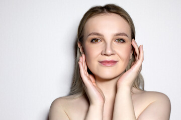 Beauty portrait with hands in the frame of a young girl with heterochromia and light makeup on a white background. Beauty and self-care concept.