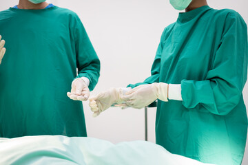 Asian surgeons team in green scrubs and masks discussing procedure in operating room. Medical professionals preparing for surgery, showcasing focus, communication, and teamwork in sterile environment.