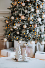 White ceramic trees in front of a beautifully decorated Christmas tree indoors