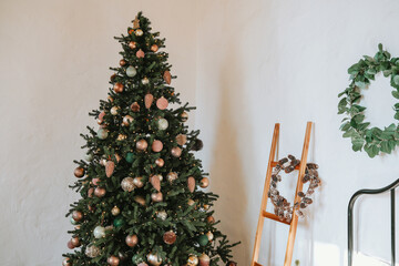Christmas tree decorated with ornaments beside a wooden ladder and wreath