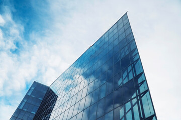A modern office building reflecting clouds against a bright blue sky in an urban setting