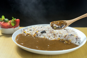 湯気の立つ雑穀とカレーをスプーンですくう
