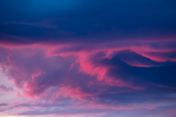 Ciemna, kłębiasta chmura oświetlona czerwonymi promieniami zachodzącego słońca. © boguslavus