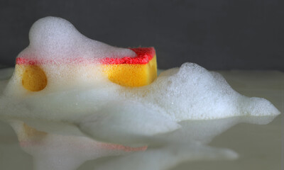 Fototapeta premium Red dishwashing sponge in soap suds and bubbles for cleaning and washing design
