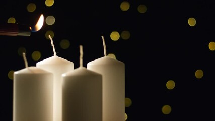 Hand lightning the first Advent candle, four white candles on a bokeh festive background, close up shot. Christmas, celebration, and holidays concepts.